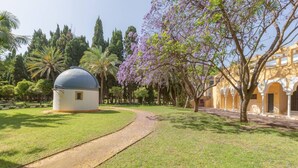 Un patio con una pequeña estructura en forma de cúpula, un sendero y un edificio con arcos.