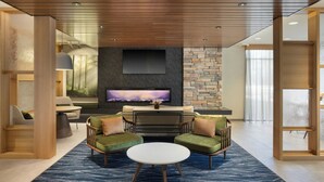 A modern living room with a flat-screen TV, green upholstered chairs, a white coffee table, and a stone accent wall. - Fairfield by Marriott Inn & Suites Oxford (Oxford)