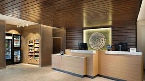A hotel reception area with a wooden reception desk, a digital screen, and a refrigerator stocked with beverages. - Fairfield by Marriott Inn & Suites Oxford (Oxford)