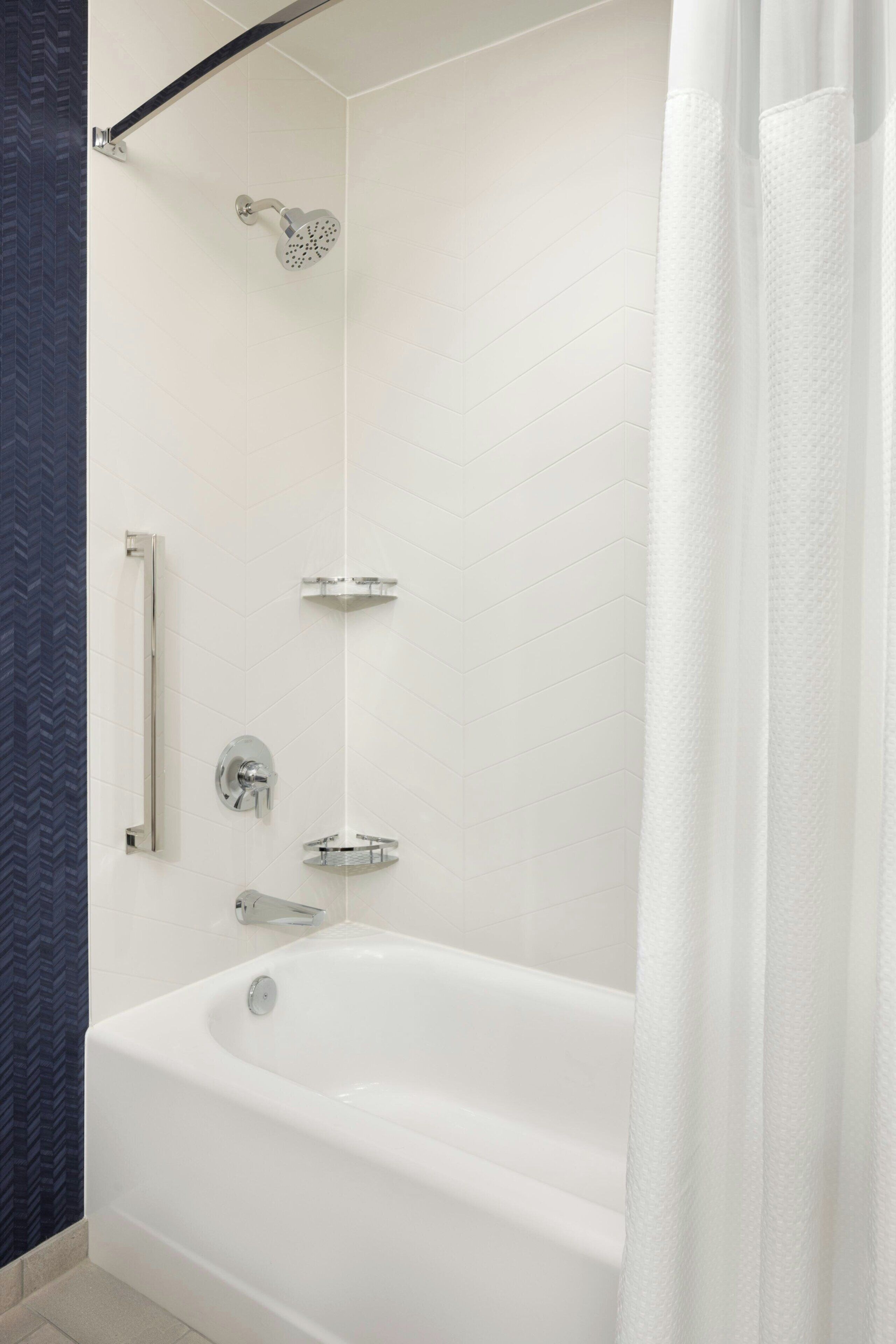 Un baño moderno con una bañera blanca, un cabezal de ducha de mano, un perchero de pared y un panel de control de ducha.