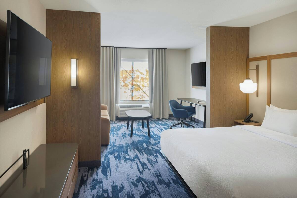 Habitación de hotel con cama, escritorio, silla, televisor y ventana con cortinas.