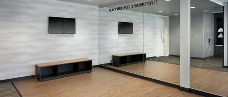 A modern room with a wooden floor, a bench, a wall-mounted TV, and a mirror reflecting the room.
