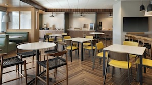A modern dining area with multiple tables and chairs, a kitchen in the background, and a flat-screen TV mounted on the wall. - Fairfield by Marriott Inn & Suites Oxford (Oxford)