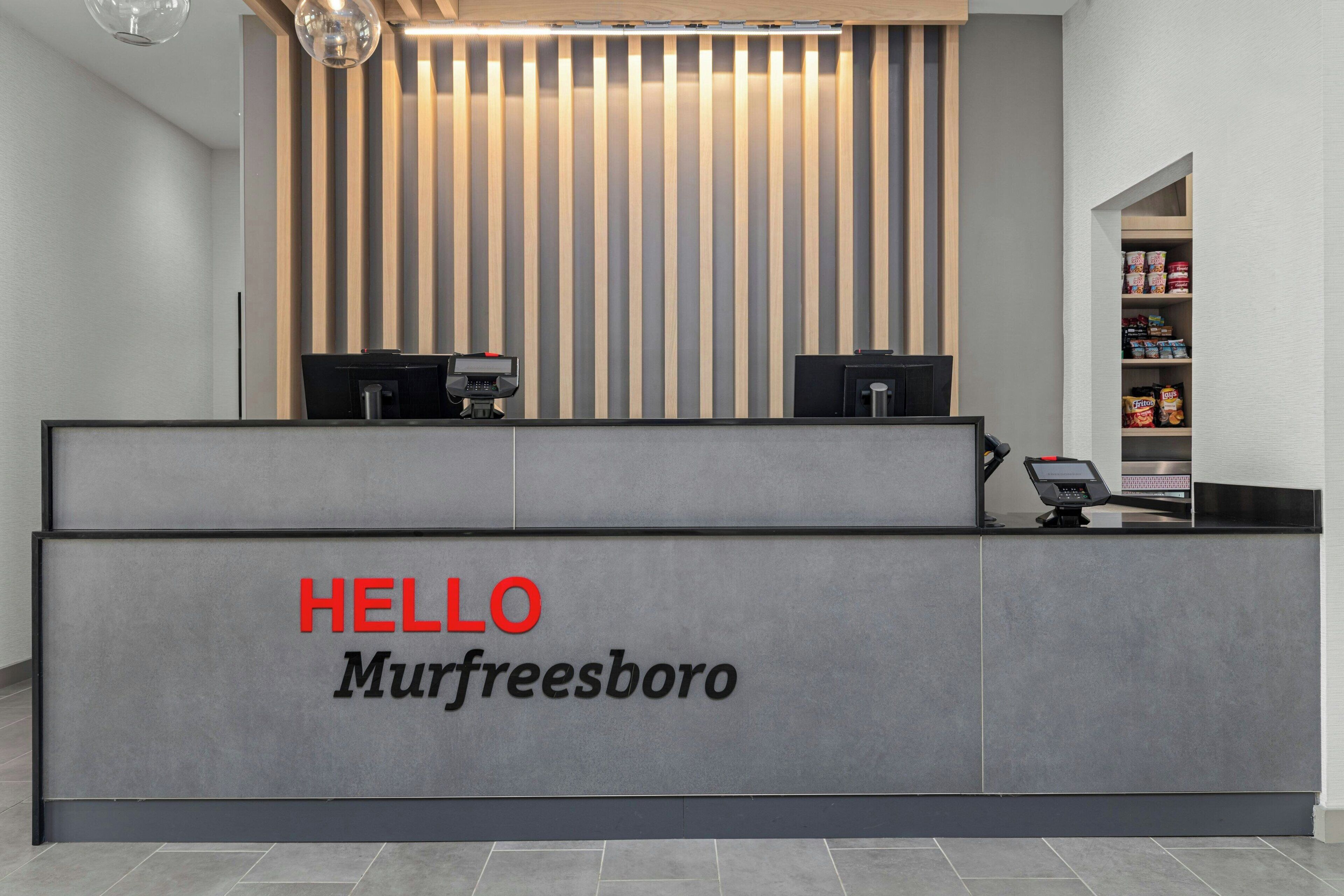 A reception desk with a 'HELLO Murfreesboro' sign, two computer monitors, and a shelf with various items.