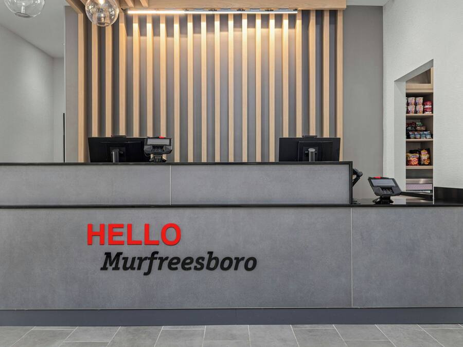 A reception desk with a 'HELLO Murfreesboro' sign, two computer monitors, and a shelf with various items.