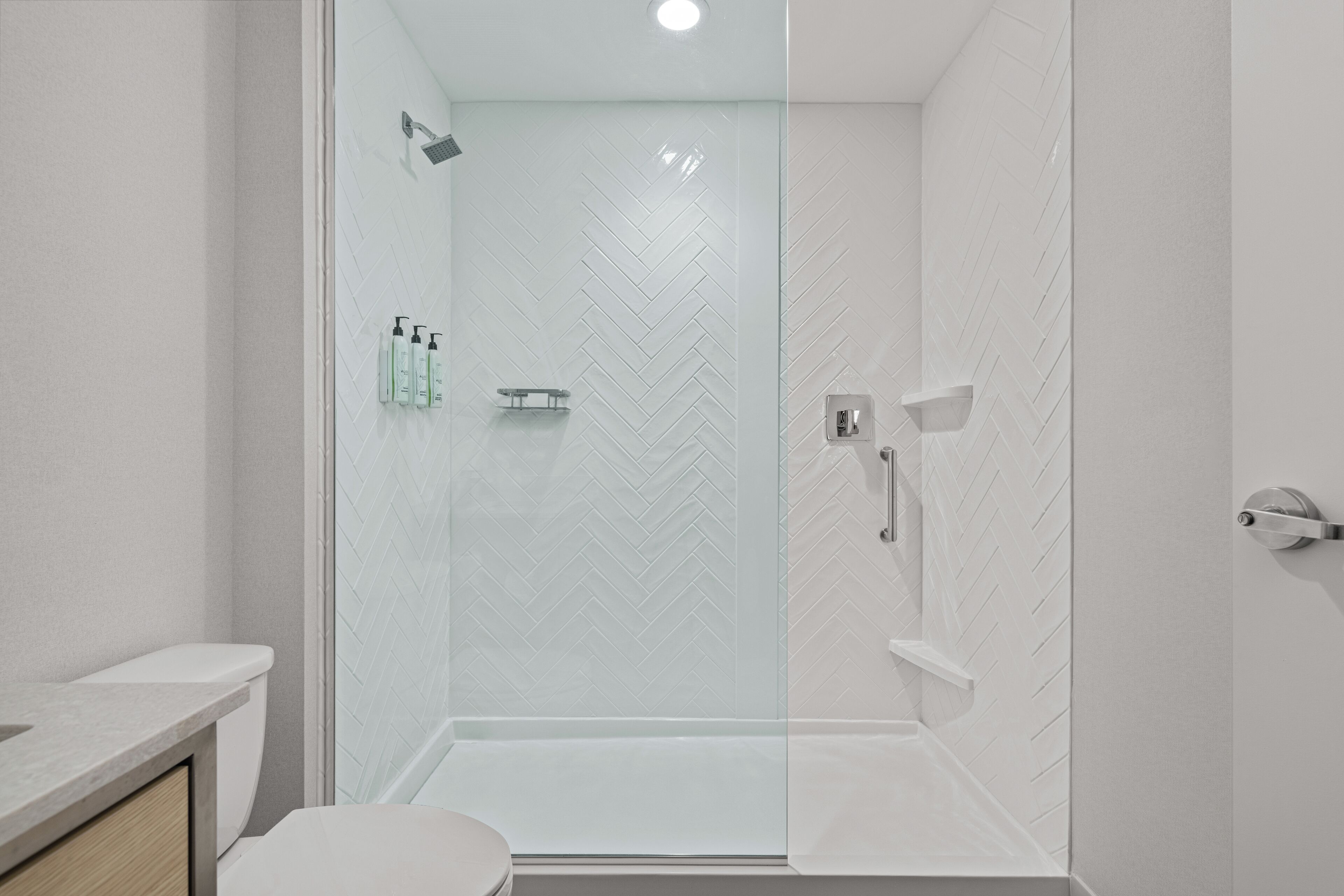 A modern bathroom with a glass shower enclosure, white herringbone-patterned tiles, and a white toilet.