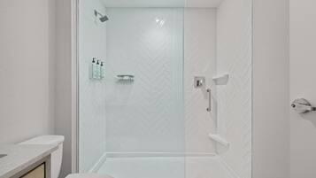 A modern bathroom with a glass shower enclosure, white herringbone-patterned tiles, and a white toilet.