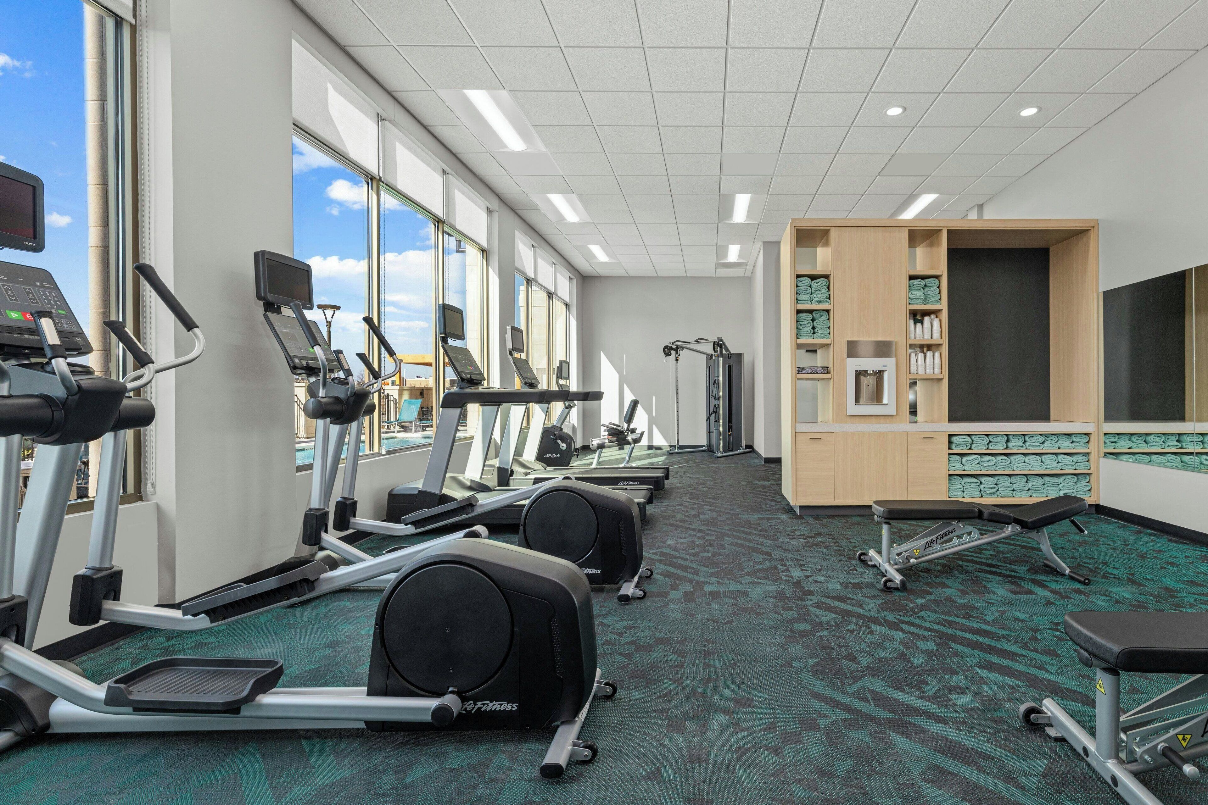 Une salle de sport équipée de tapis de course, de vélos elliptiques et d’un banc de musculation.