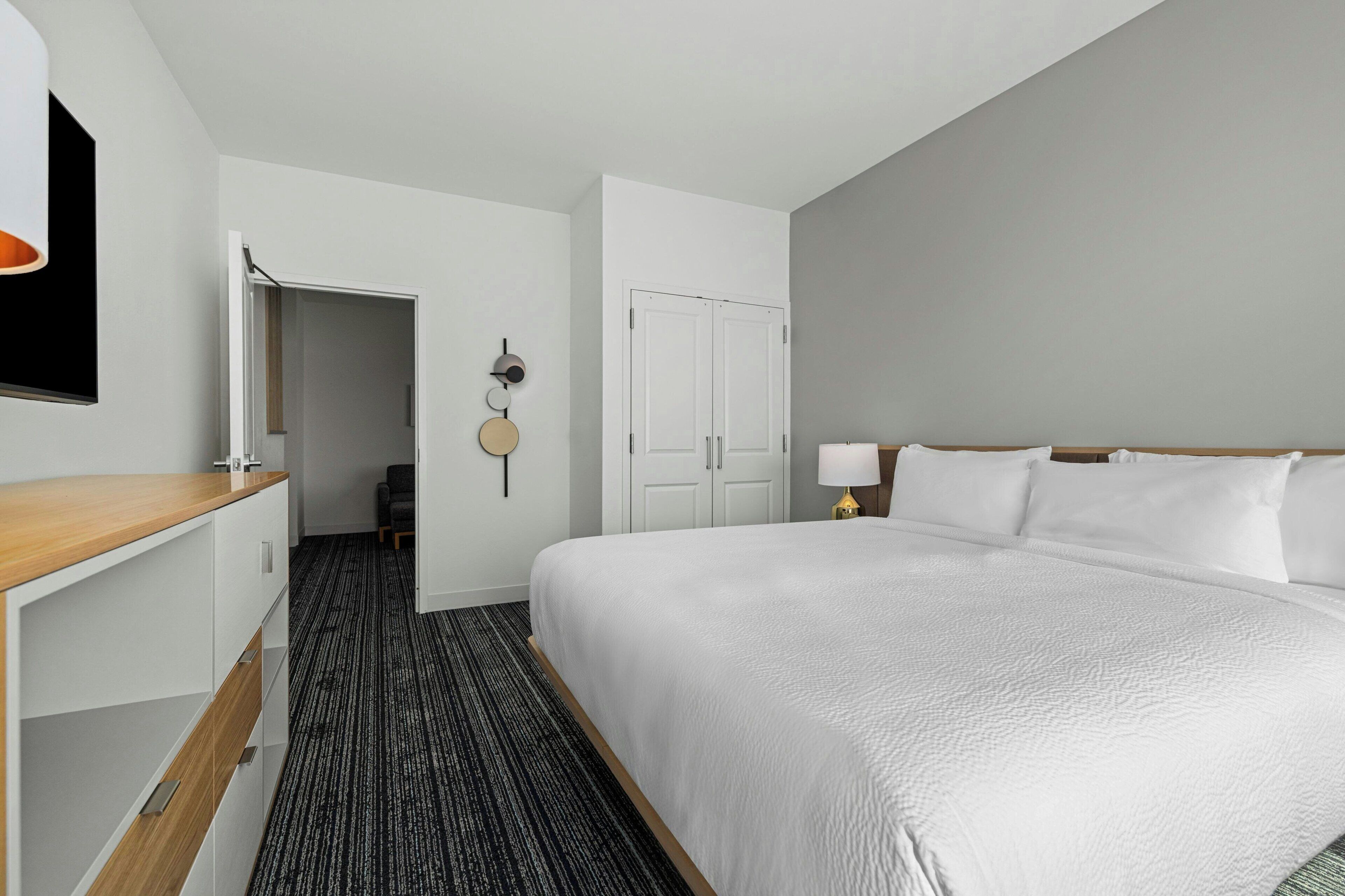 A hotel room with a large bed, a desk, a wardrobe, and a door leading to a hallway.