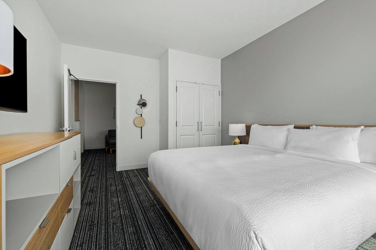 Habitación de hotel con una cama grande, un escritorio, un armario y una puerta que da a un pasillo.