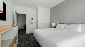A hotel room with a large bed, a desk, a wardrobe, and a door leading to a hallway.