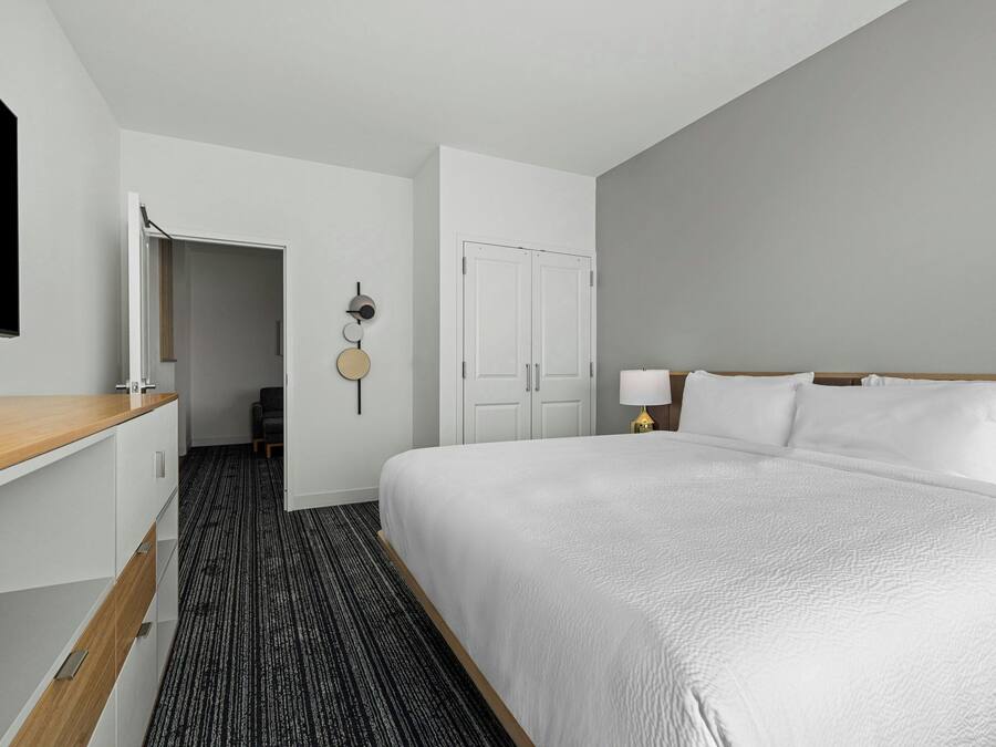 A hotel room with a large bed, a desk, a wardrobe, and a door leading to a hallway.