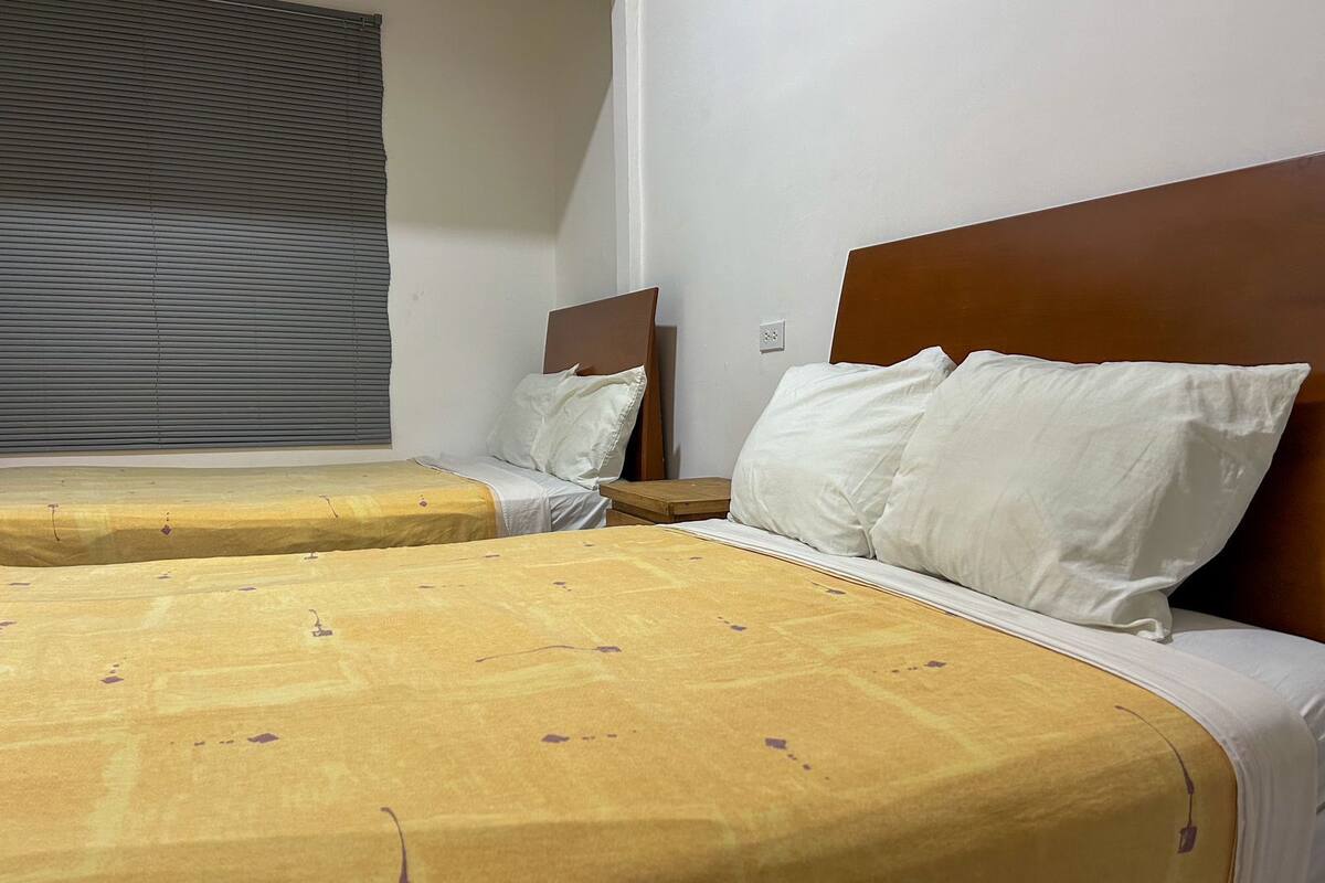 Habitación de hotel con dos camas, cada una con cabecero de madera, y una ventana con persianas.