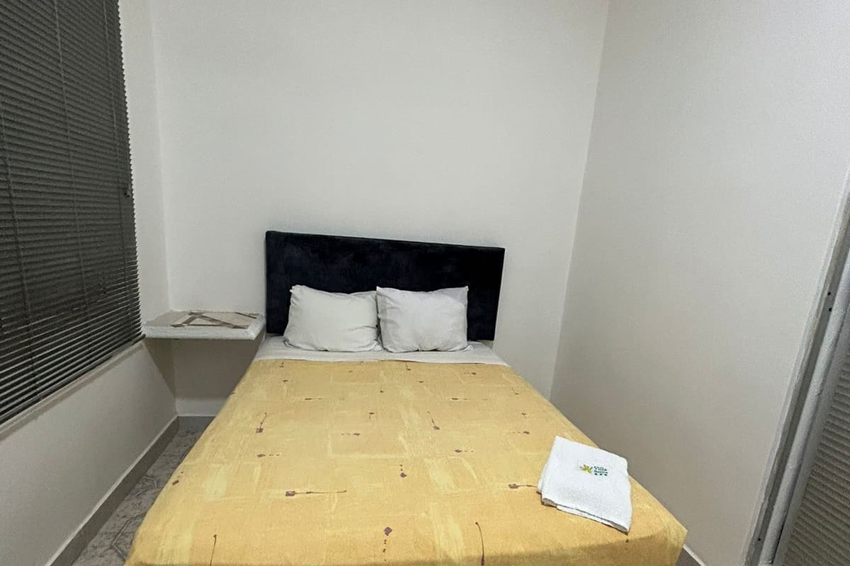 Una cama pequeña y bien hecha con una colcha amarilla y un almohadón blanco.