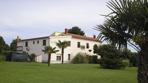 A two-story building with a white facade and red-tiled roof, surrounded by a well-maintained lawn and palm trees. - ROOMS MATEA PULA (Vodnjan)