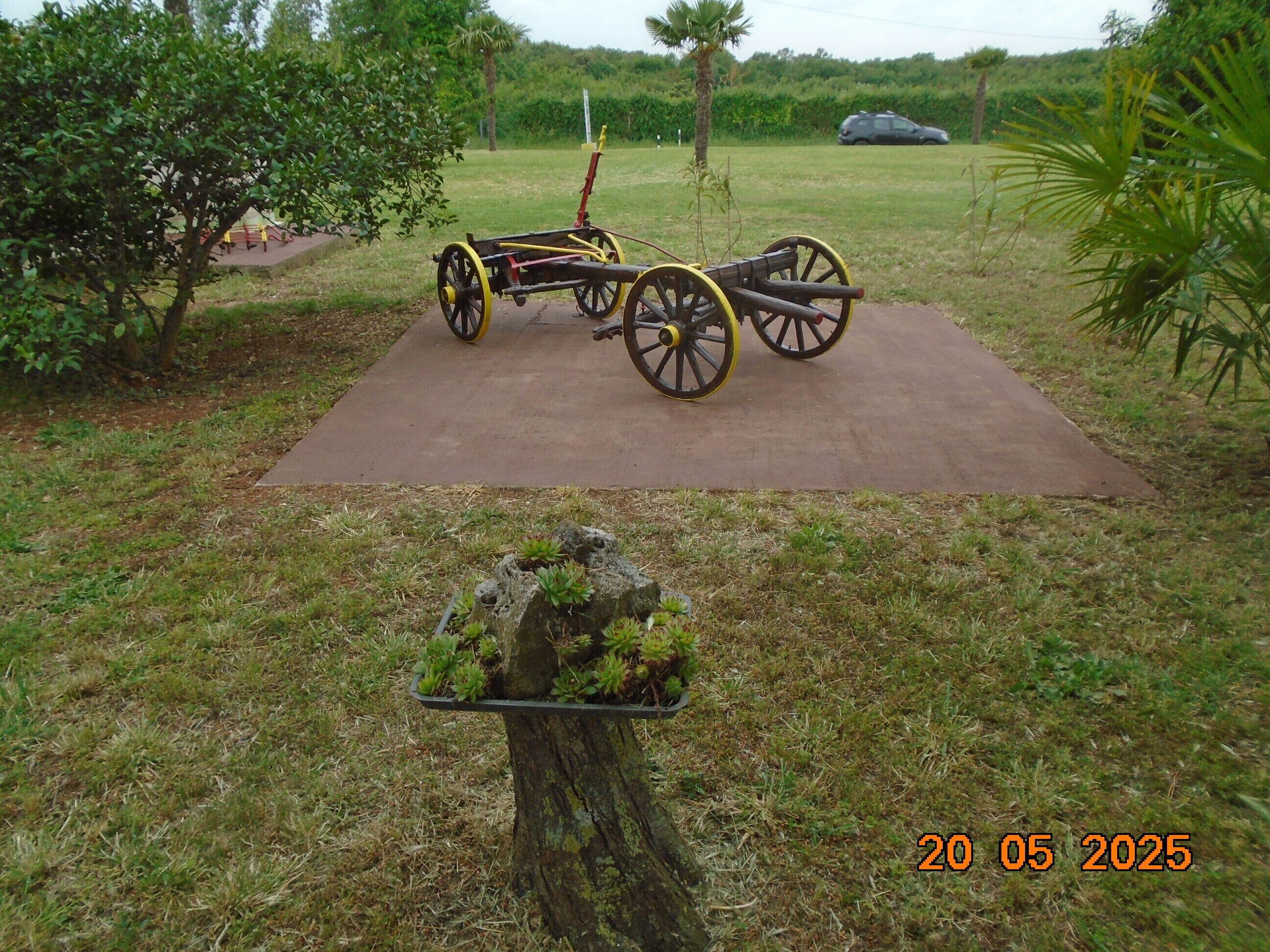 A cart with yellow wheels on a paved area surrounded by grass and trees.