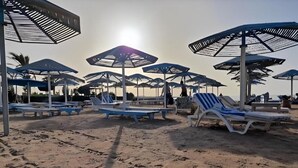 A beach with sun umbrellas and lounge chairs. - Home from home 1 bedroom apartment with AC & WiFi in fantastic Al dora compound (Red Sea Governorate)