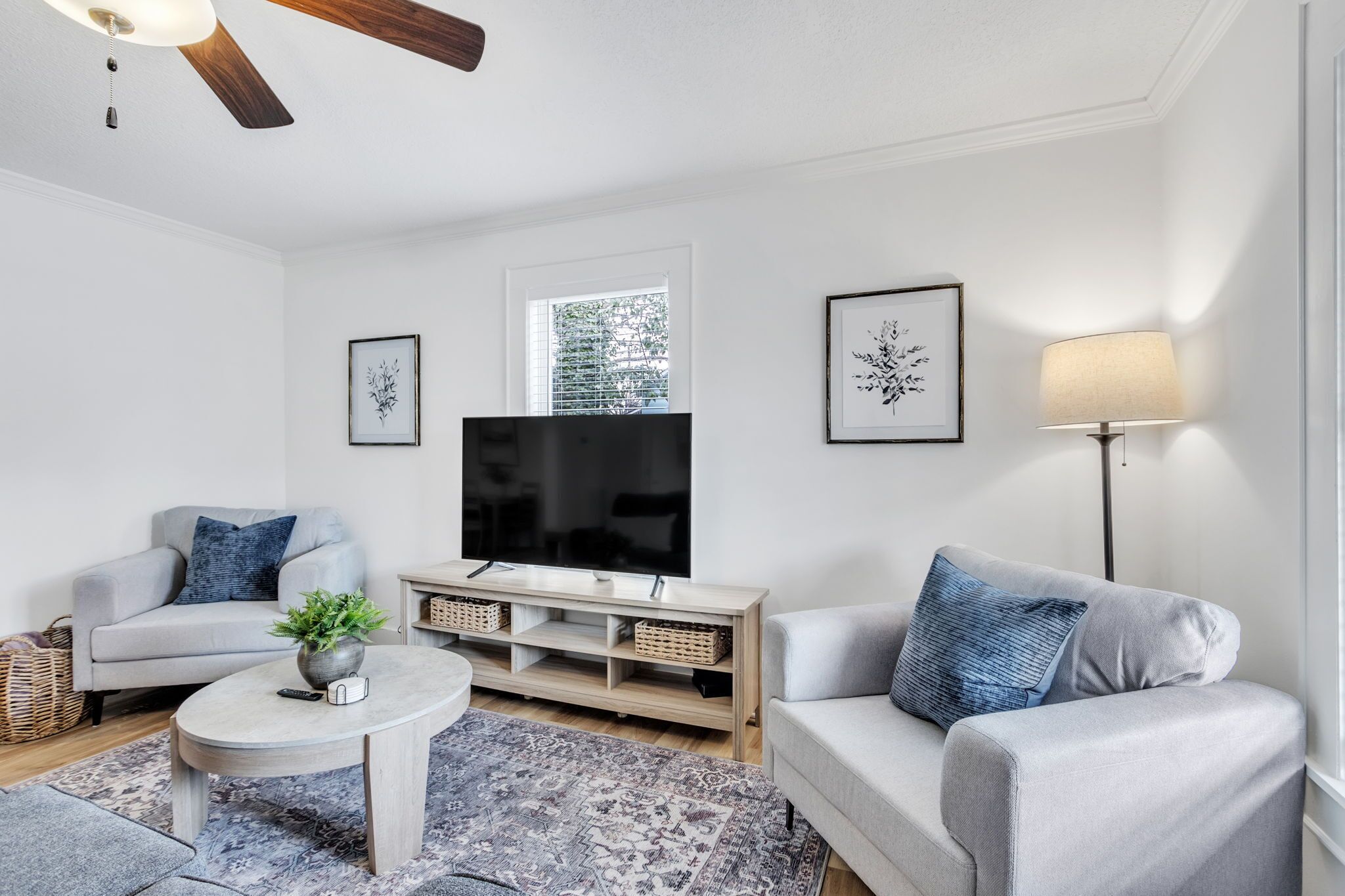 Ein modernes Wohnzimmer mit Flachbildfernseher, grauen Sofas, einem Couchtisch und einer Stehlampe.