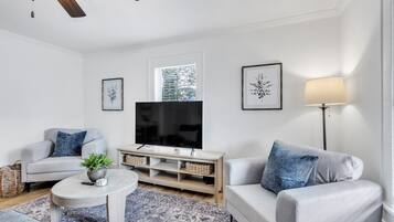 Ein modernes Wohnzimmer mit Flachbildfernseher, grauen Sofas, einem Couchtisch und einer Stehlampe.