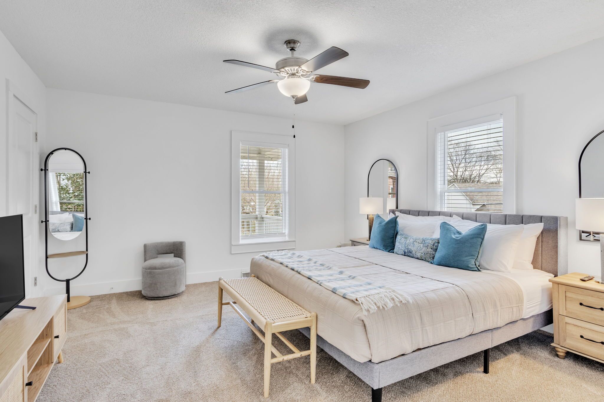 A bedroom with a bed, a ceiling fan, a bench, a TV, and a bedside table.