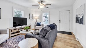 Ein modernes Wohnzimmer mit Fernseher, Deckenventilator, grauem Sofa, Couchtisch und einem TV-Schrank mit Pflanze.