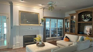 A living room with a fireplace, a ceiling fan, and a large window. - Charming Masters Rental: 5BR Home Near Augusta National (Martinez)