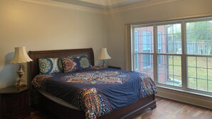 A bedroom with a large bed, two bedside lamps, a ceiling fan, and a large window with a view of the outside. - Charming Masters Rental: 5BR Home Near Augusta National (Martinez)