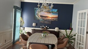 A dining room with a round table, six chairs, a chandelier, a large wall painting, and a door with glass panels. - Charming Masters Rental: 5BR Home Near Augusta National (Martinez)