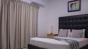 Una cama bien hecha con una colcha a rayas, un cabecero oscuro y una mesita de noche con una lámpara.