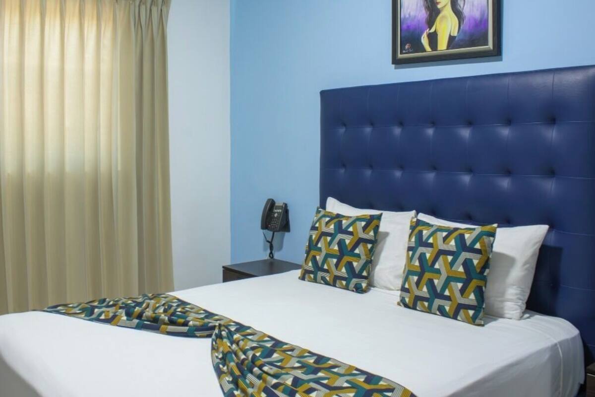 A hotel room with a large bed, a blue headboard, and patterned pillows.