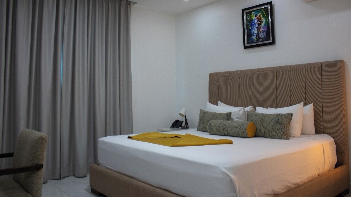 A hotel room with a large bed, a bedside table, a chair, and a painting on the wall.