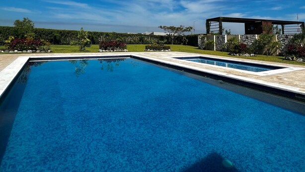 Una piscina rectangular con borde de piedra, rodeada por un jardín ajardinado con diversas plantas y un muro de piedra.