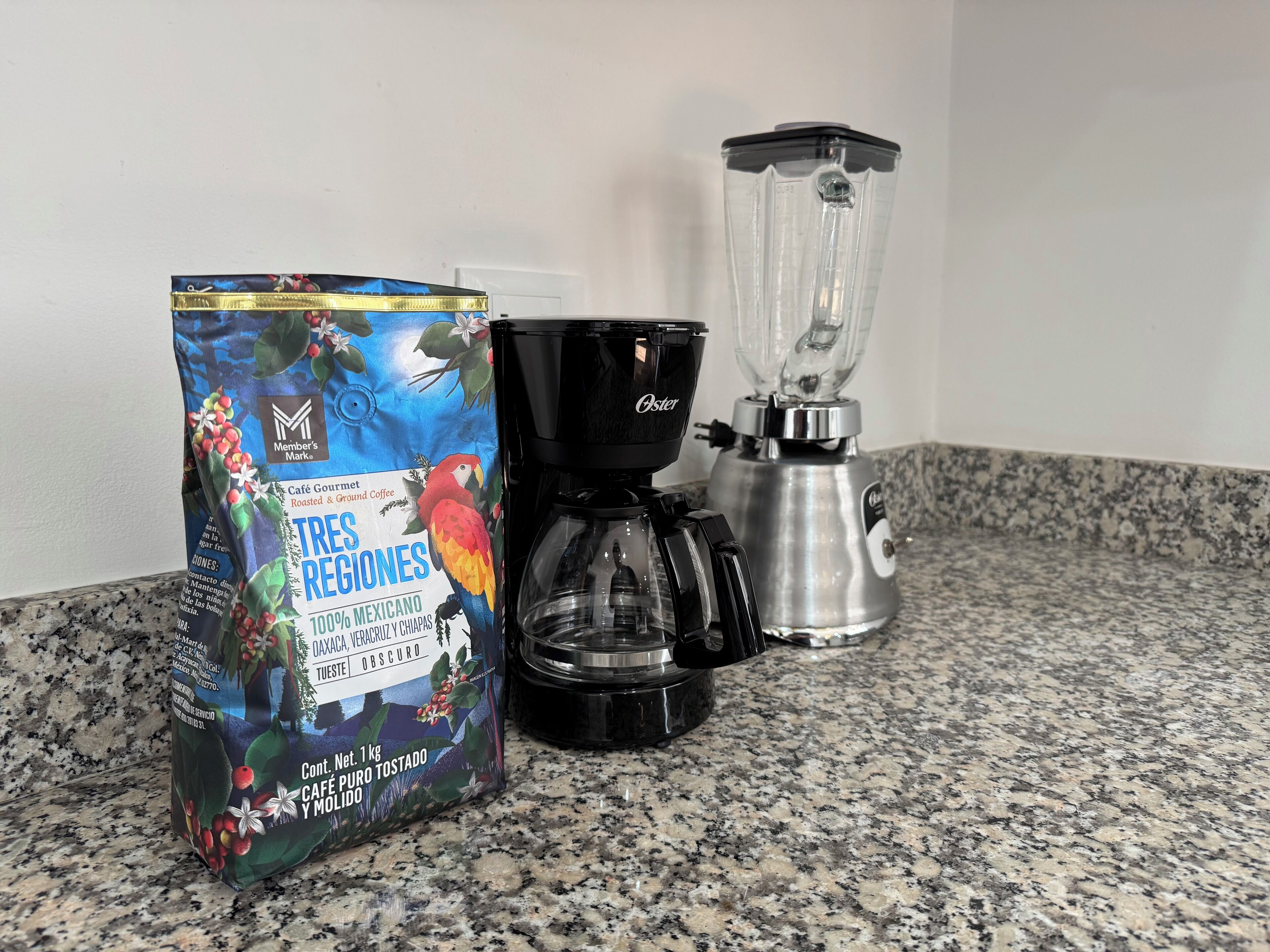 Um saco de café, uma cafeteira e um liquidificador em uma bancada de granito.