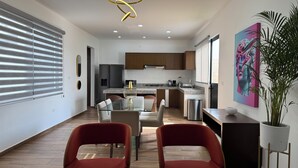 Una cocina moderna con una isla central, un comedor con dos sillas rojas y una planta grande en maceta.