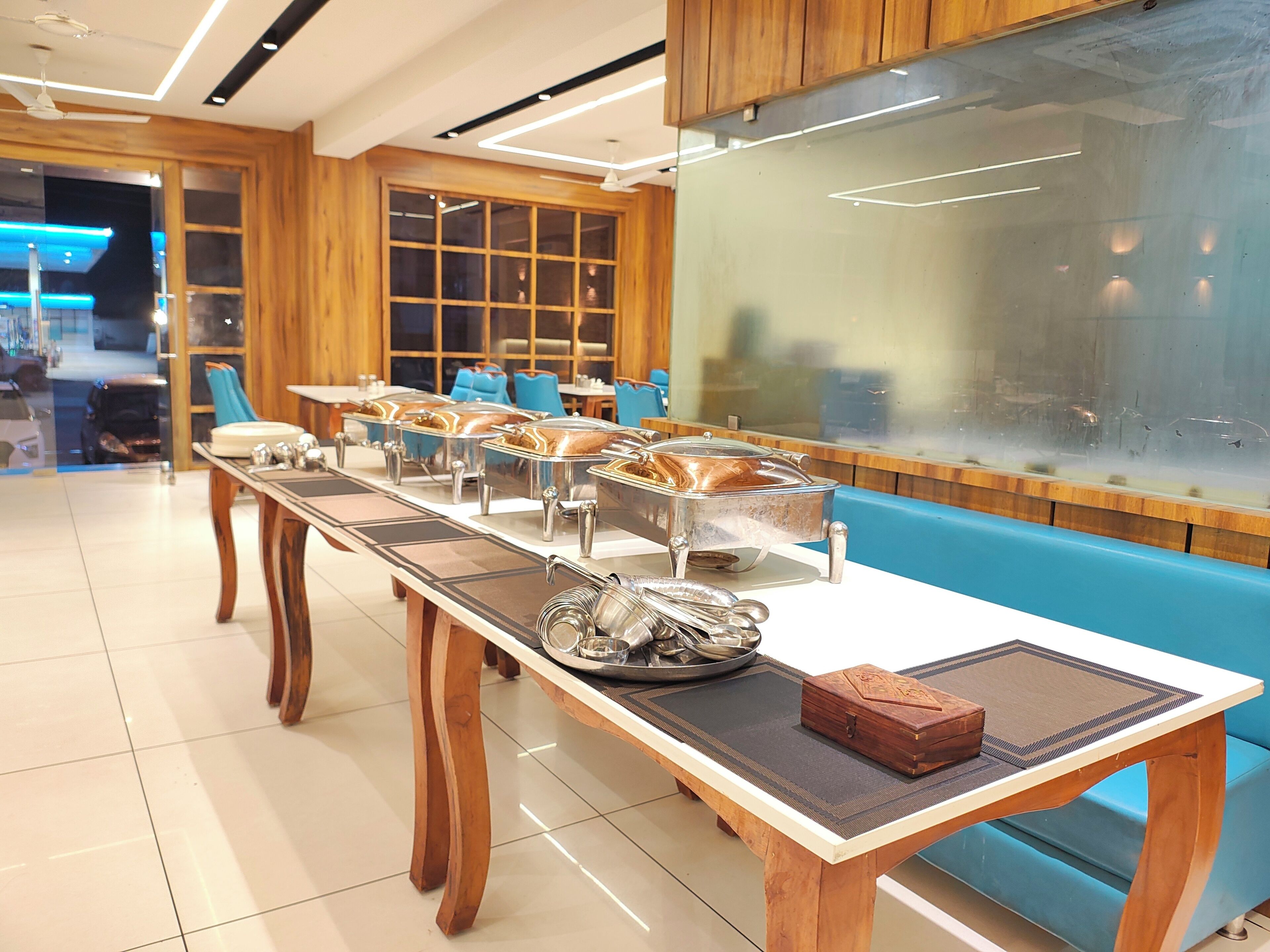 Un comedor moderno con una larga mesa de madera, asientos acolchados en azul y un separador de vidrio.