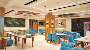 A modern restaurant with blue chairs, wooden tables, and a green wall decoration. - Aceotel Premier TK Morbi (Morbi)