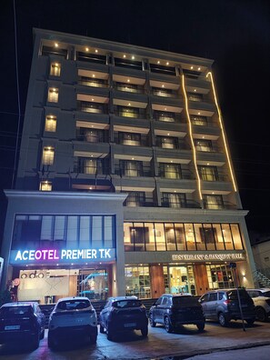 A multi-story hotel with a prominent sign for "Aceotel Premier T.K" and a "Restaurant & Banquet Hall" below. Several cars are parked in front.