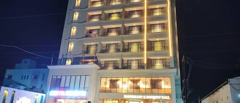 A multi-story hotel with a well-lit entrance and several parked cars in front.