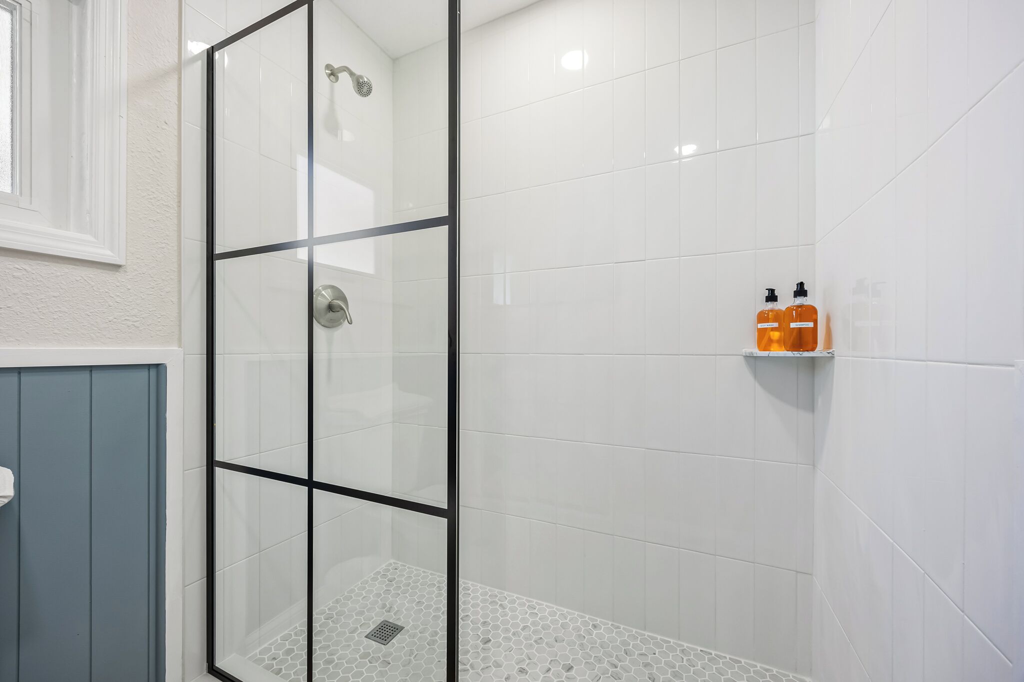A glass-enclosed shower with white tiles and a small shelf with toiletries.