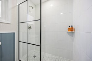 A glass-enclosed shower with white tiles and a small shelf with toiletries. - The Drift (Cocoa Beach)