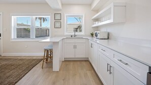 A modern kitchen with white cabinetry, a built-in microwave, and a window with blinds. - The Drift (Cocoa Beach)