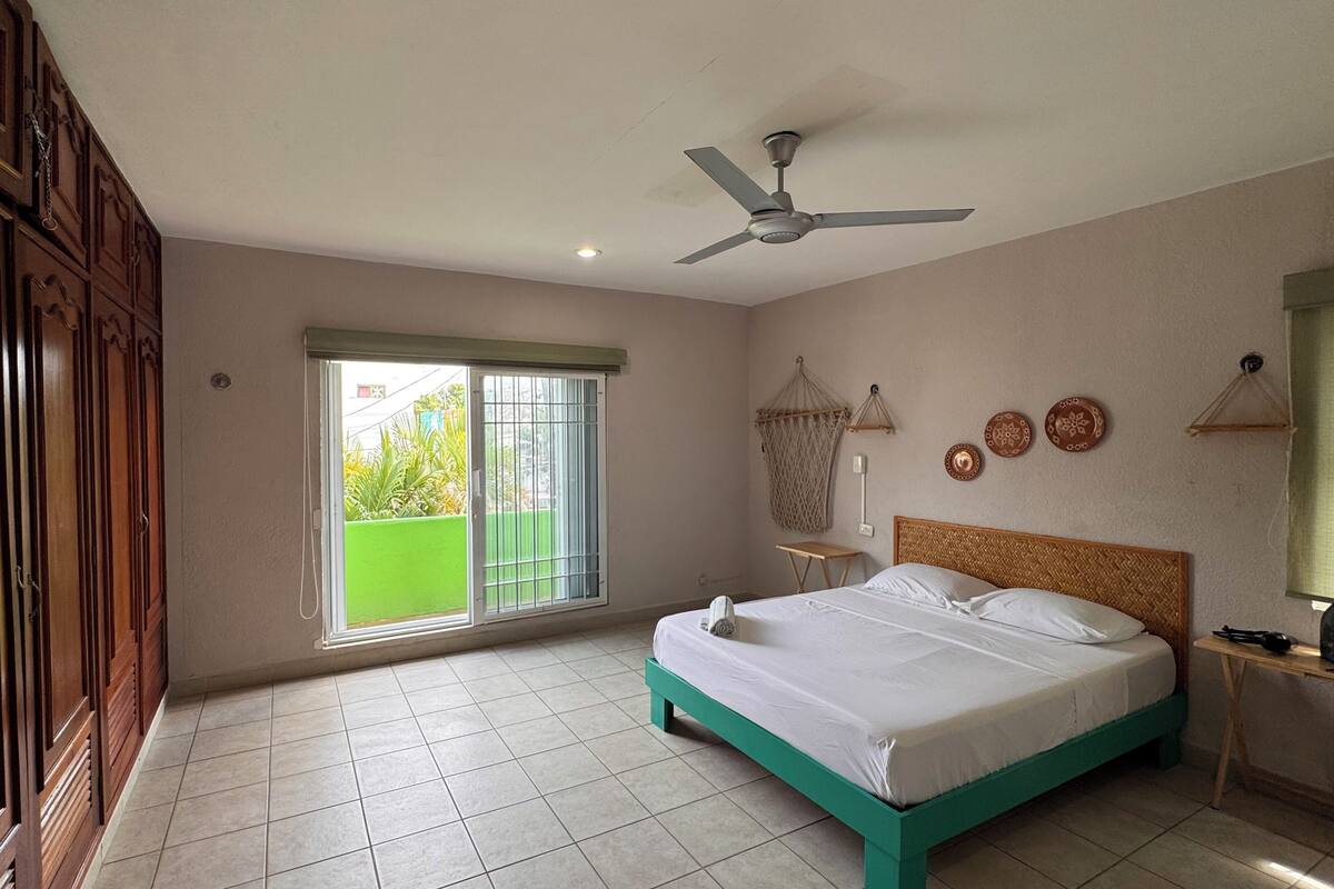 A bedroom with a bed, a ceiling fan, a window with a view, and a door with a decorative handle.