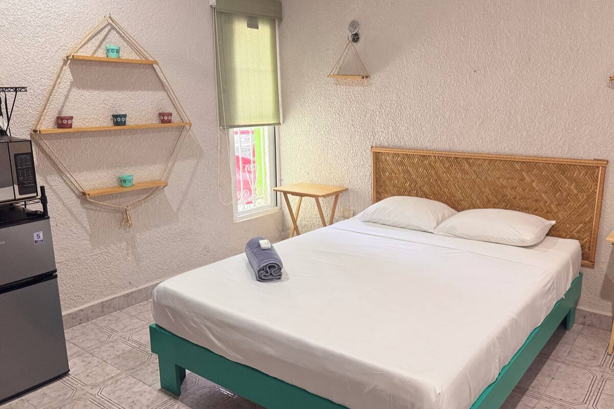 A neatly arranged hotel room with a bed, a small table, a shelf with toiletries, and a window with a view.