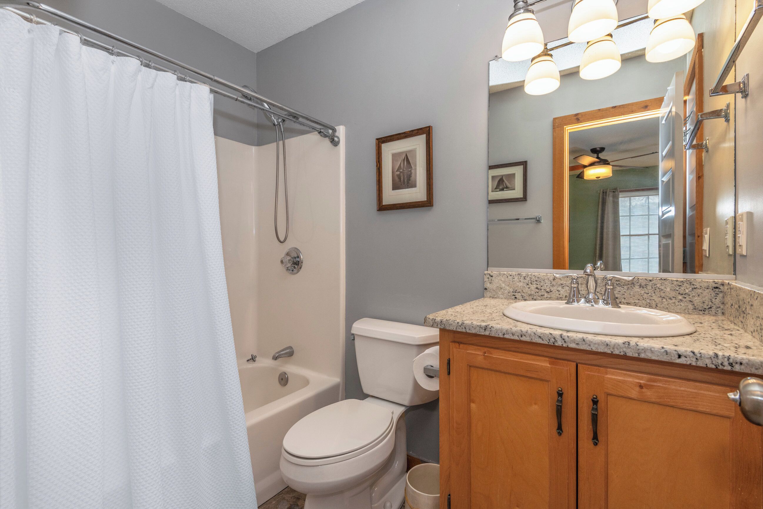 A bathroom with a shower curtain, a bathtub, a toilet, a sink, and wooden cabinets.