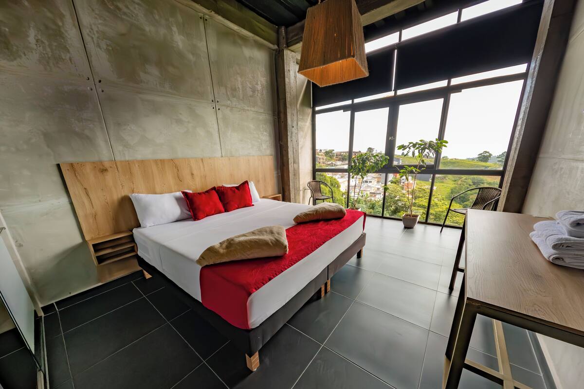 A modern hotel room with a large bed, a wooden headboard, a view of the city, and a small table with towels.