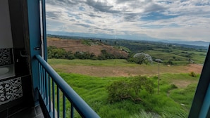 Un balcón con vistas a un paisaje verde y colinas lejanas bajo un cielo nublado.