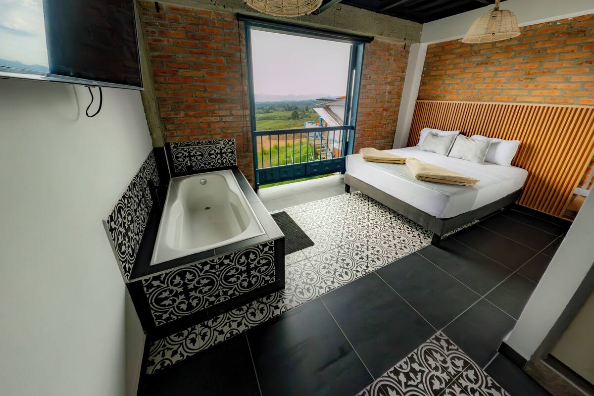 A modern bathroom with a bathtub, a balcony with a view, and a bed with white bedding.