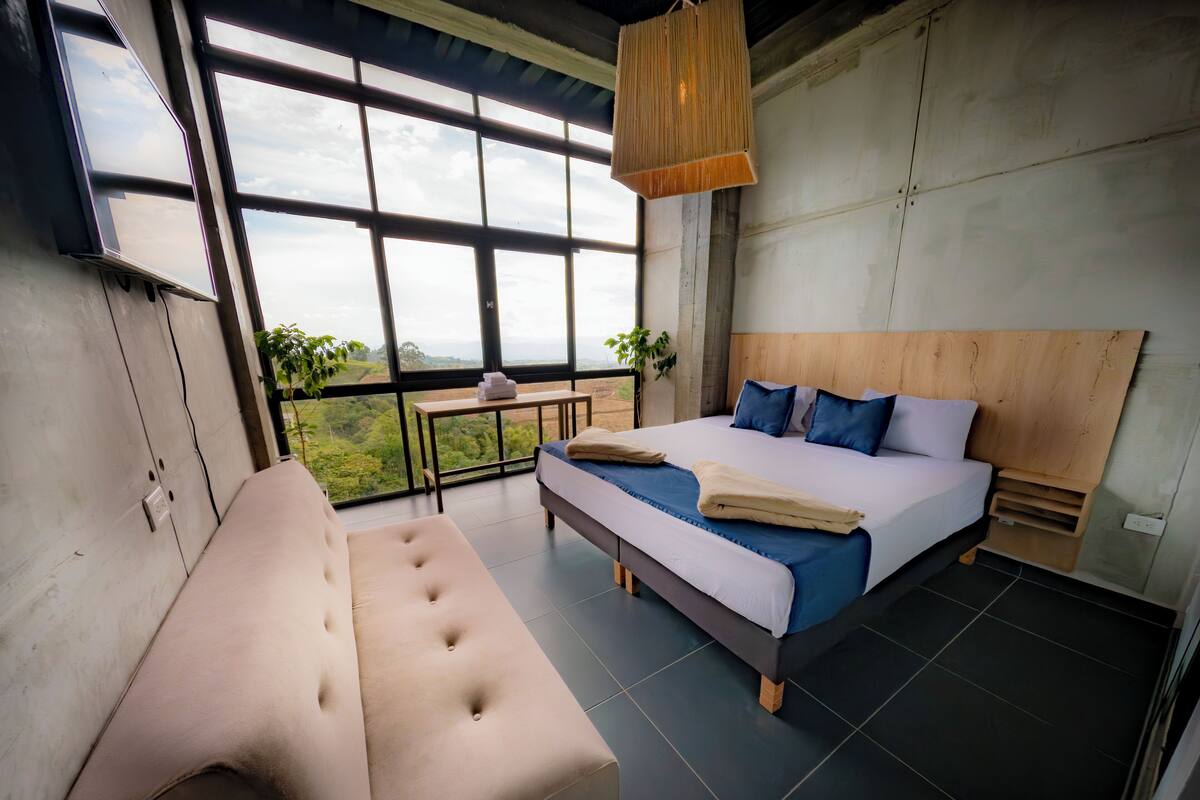 A modern bedroom with a large bed, a sofa, and a view of the outdoors.