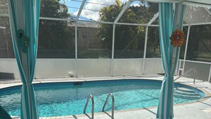 A swimming pool with a glass enclosure, a pool ladder, and a lounge area with a patterned rug. - Charming 2-bedroom pool home with AC, WiFi in Lehigh Acres (Lehigh Acres)