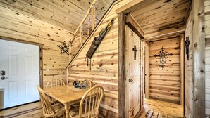 A wooden interior with a dining table and chairs, a staircase, and a door with a cross. - Rustic Cabin On 31 Acres + Near the Frio River • Pet Friendly • Sleeps 6+ (Sabinal)